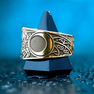 May include: A gold ring with a crescent moon design and intricate details. The ring is on a black pyramid-shaped stand.