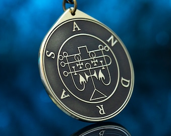 May include: A brass pendant with a black sigil and the letters "SANDR" around the edge. The sigil is a complex design with geometric shapes and symbols.