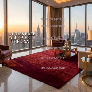 Deep wine color solid area rug displayed in a luxury modern living room with large windows and city views. Plush handcrafted rug with rich burgundy tone adds warmth and elegance to contemporary interior decor. Perfect for living room, bedroom, or apartment styling, this handmade rug features a smooth, soft texture and premium finish, ideal for modern, minimalist, and luxury home interiors.
