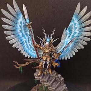 May include: A miniature figurine of a warrior with large, blue and white feathered wings, holding two swords. The warrior is clad in gold armor and stands on a stone base. The wings are spread wide, and the figure is posed dynamically.
