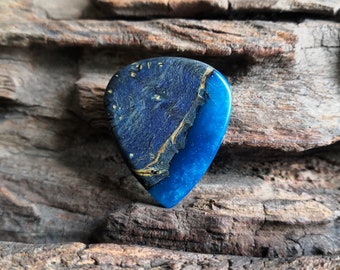 May include: A blue and gold guitar pick with a unique marbled design. The pick is made of wood and resin and has a smooth, polished finish.