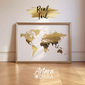 Op de afbeelding: Een ingelijste wereldkaartprint met goudfoliedetails op een witte achtergrond. De kaart staat in een gouden lijst en heeft de tekst "Real Foil" erboven. De onderkant van de lijst heeft de tekst "Artara DARA".