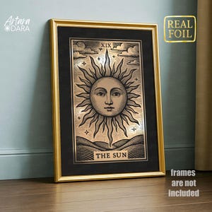 May include: Framed artwork featuring a sun design from a tarot card. The image has a gold frame and a black mat. The sun illustration is in a copper color with the words "THE SUN" at the bottom. The text "REAL FOIL" is in the upper right corner.