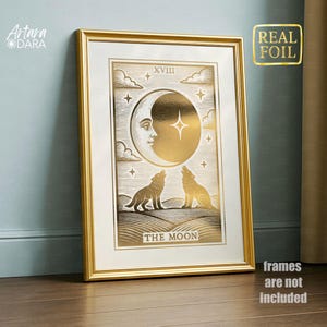 May include: Gold-framed art print featuring a gold foil illustration of the moon with a face, stars, and two howling wolves. The text "THE MOON" is at the bottom. The print is labeled "REAL FOIL" and "frames are not included".