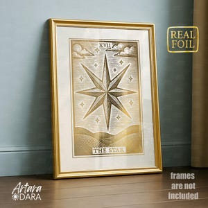 May include: A framed gold foil print of "The Star" tarot card. The artwork features a large eight-pointed star, clouds, and the Roman numeral XVII. The frame is gold, and the print has a gold foil finish. The words "Real Foil" are in a gold sticker on the right.