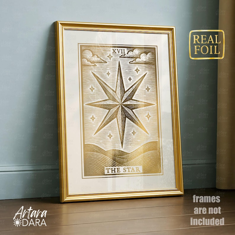 May include: A framed gold foil print of "The Star" tarot card. The artwork features a large eight-pointed star, clouds, and the Roman numeral XVII. The frame is gold, and the print has a gold foil finish. The words "Real Foil" are in a gold sticker on the right.
