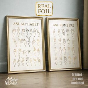 May include: Two framed wall art prints featuring gold foil American Sign Language charts. The left print displays the ASL alphabet from A to Z, while the right print shows ASL numbers from 1 to 20. Both prints feature hand illustrations.