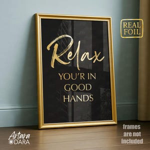 May include: A framed art print with a gold frame and a black background. The words "Relax, You're in Good Hands" are written in gold foil. The print is leaning against a wall.