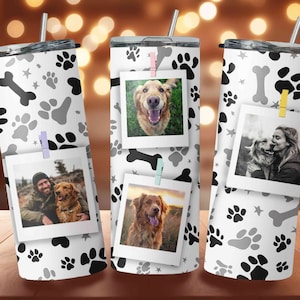 May include: Three stainless steel tumblers with a white background and a pattern of black paw prints and bones. Each tumbler has a photo of a dog clipped to it with miniature clothespins.