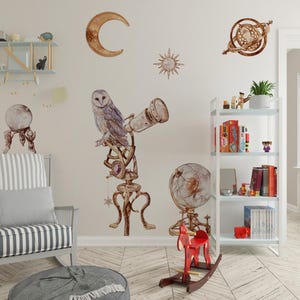 Pode incluir: Um conjunto de autocolantes de parede com ilustrações em aguarela de uma coruja sobre um telescópio, uma lua crescente, um sol, uma esfera armilar, uma bola de cristal num suporte e um globo, em tons de castanho e dourado.