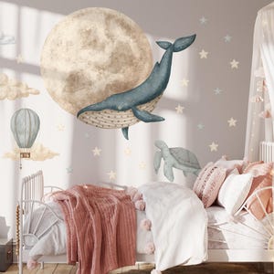 May include: A set of wall decals featuring a large textured moon, a blue whale, a sea turtle, a hot air balloon, and various clouds and stars. The illustrations are rendered in soft, muted tones, designed to be applied to a flat wall surface.