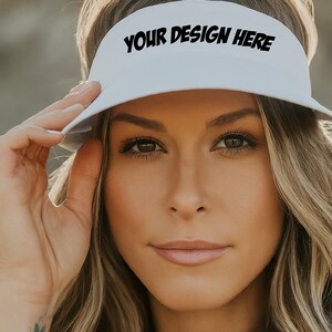 May include: A white visor with the text "YOUR DESIGN HERE" in black lettering. The visor is being worn by a person with long blonde hair.