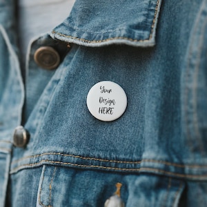 May include: A white button with the text "Your Design Here" pinned to a blue denim jacket.