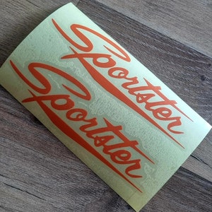 Könnte beinhalten: Zwei orangefarbene Vinyl-Aufkleber mit dem Wort "Sportster" in einer stilisierten Schrift.