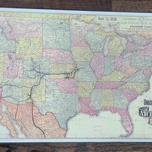 May include: A vintage-style map of the United States featuring the Atchison, Topeka and Santa Fe Railroad routes. The map displays states in pastel colors, black rail lines, a compass rose, and text reading A Correct Map of the United States-America.
