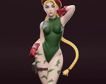 May include: A figurine of a female character in a green bodysuit with camouflage-style markings. She wears a red beret, gloves, and boots. Her blonde hair is styled in a long braid. The figure is posed on a round black base.