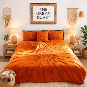 May include: An orange duvet cover set with a sunburst design, including matching pillow shams and a decorative pillow. The text "THE URBAN DUVET" is displayed in a framed print above the bed. The room is decorated in a bohemian style.