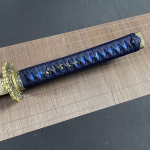 May include: A black and blue katana sword with a gold-coloured handle and a decorative design. The handle is wrapped in black cord with blue accents.