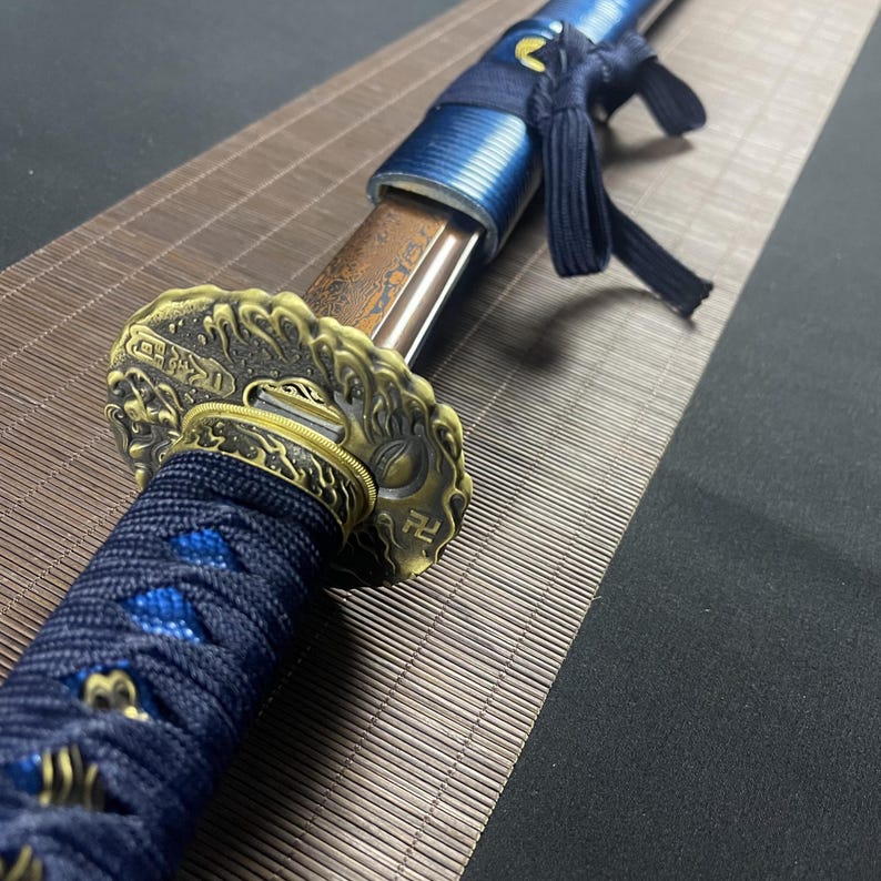May include: A close-up of a katana sword with a blue and gold scabbard. The scabbard is decorated with a wave pattern and the kanji for "sword".