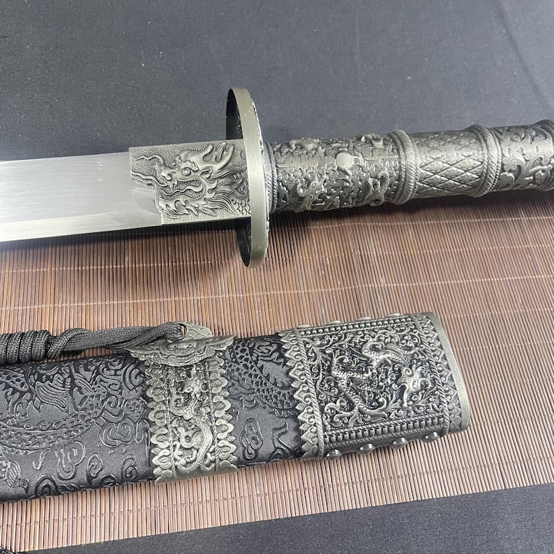 May include: A silver-coloured sword with a black scabbard. The sword has a dragon design on the handle and the scabbard has a dragon design on the front.