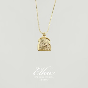 May include: A gold necklace with a textured bread pendant. The pendant is shaped like a slice of bread.