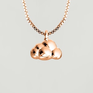 Puede incluir: Un collar de oro rosa con un colgante en forma de nube. El colgante está hecho de varias formas redondeadas que se unen para formar una nube.