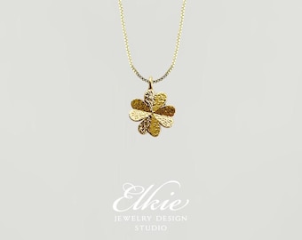 May include: A gold necklace with a four-leaf clover pendant. The clover is textured and has a hammered finish.