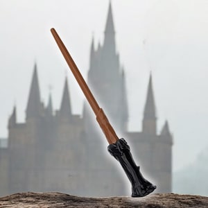 May include: A brown and black wand with a detailed handle, against a blurry background of a castle.