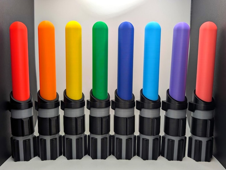 K&ouml;nnte beinhalten: Eine Sammlung von acht farbigen Lichtschwertern mit unterschiedlich farbigen Klingen: rot, orange, gelb, gr&uuml;n, blau, hellblau, lila und pink. Die Griffe sind schwarz und grau.