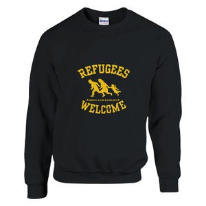 以下が含まれることがあります： 家族3人が歩いている「Refugees Welcome」という黄色のグラフィックデザインが施された黒いスウェットシャツ。家族の下のテキストには「Bring your families」と書いてあります。