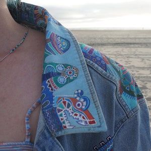 May include: A denim jacket with a colorful patterned collar. The collar is made of a light blue fabric with a variety of geometric shapes and designs in shades of blue, green, red, and white.
