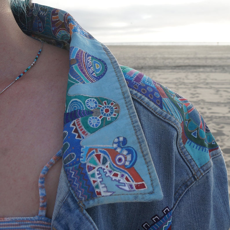 May include: A denim jacket with a colorful patterned collar. The collar is made of a light blue fabric with a variety of geometric shapes and designs in shades of blue, green, red, and white.