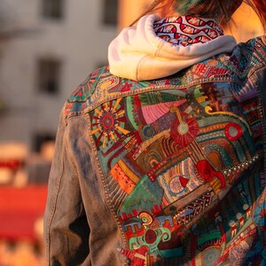 May include: A denim jacket with a colorful, abstract design painted on the back. The design features geometric shapes, swirls, and lines in shades of red, blue, green, yellow, and orange.