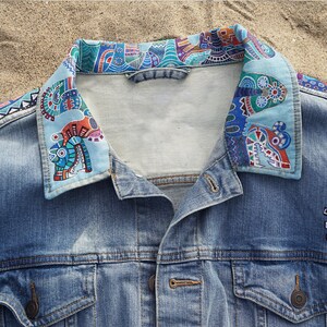 May include: A blue denim jacket with a colorful patterned collar. The collar is made of a light blue fabric with a geometric design in shades of blue, green, red, and orange.