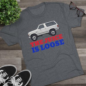 May include: A gray t-shirt with a white Ford Bronco on it. The text "The Juice Is Loose" is printed in red and blue letters below the vehicle.