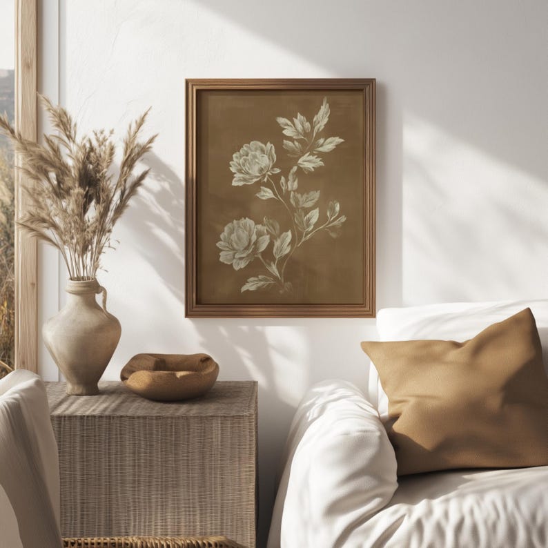 以下が含まれることがあります： 茶色の背景にクリーム色の花のイラストが描かれた、額入りの植物画。 アートワークは木製のフレームに入っており、白い壁に掛けられています。 この画像は、ホームデコレーションコレクションの一部です。