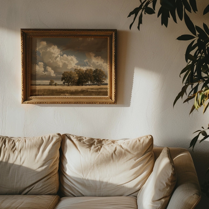 May include: A beige couch with two pillows and a throw pillow. A framed landscape painting hangs on the wall behind the couch. A green plant is in the corner of the room.