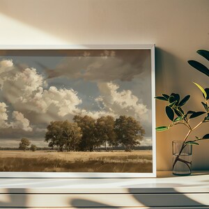 May include: A framed landscape painting of a field with trees and a cloudy sky. The painting is in a white frame and is hanging on a white wall.