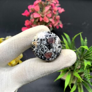 May include: A round, polished stone with a white, black, and red speckled pattern. The stone has a smooth, rounded surface and is approximately 5 cm in diameter.