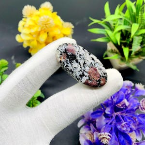 Peut inclure: Une pierre polie lisse de forme ovale avec un motif moucheté blanc, noir et rose.