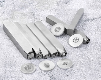 May include: A set of metal stamping tools with various designs, including a lion, skull, bee, butterfly, and a spade. The tools are arranged on a gray textured surface with sample impressions of each design.