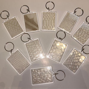 May include: Ten clear plastic keyrings with silver key rings. Each keyring has a different white patterned design.