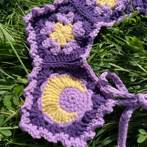 May include: A purple and yellow crocheted flower garland with a long purple and yellow crocheted tie.