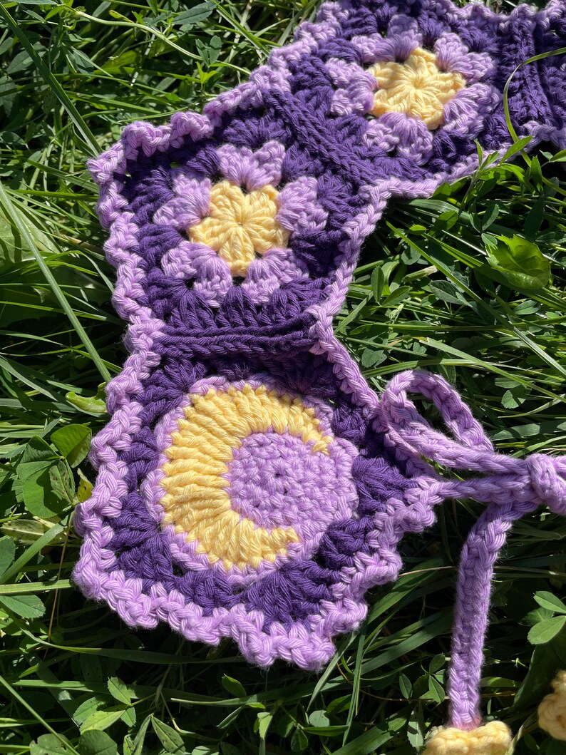 May include: A purple and yellow crocheted flower garland with a long purple and yellow crocheted tie.