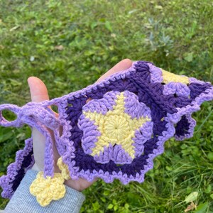 May include: A crocheted purple and yellow star-shaped garland with a yellow flower accent.