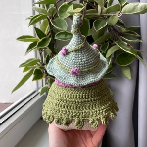 May include: A crocheted gnome doll with a green hat, pink flowers, and a green skirt.