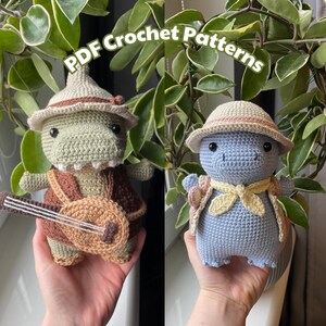 Può includere: Due giocattoli di dinosauro amigurumi all'uncinetto. Uno è verde con un gilet marrone e una chitarra, l'altro è blu con una sciarpa gialla. Entrambi indossano cappelli. Modelli di uncinetto PDF.