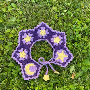 May include: A purple and yellow crocheted collar with a star, moon, and flower design. The collar has a tie closure.