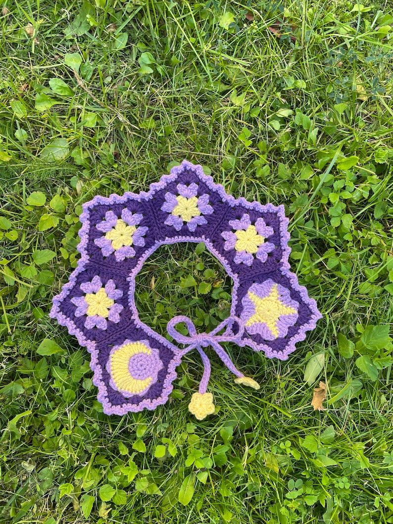 May include: A purple and yellow crocheted collar with a star, moon, and flower design. The collar has a tie closure.