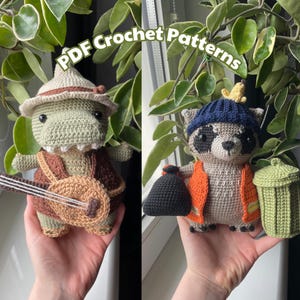 Può includere: Due giocattoli amigurumi all'uncinetto, un dinosauro verde con un cappello e un procione marrone con un cappello blu. Il dinosauro tiene una chitarra marrone e il procione tiene un sacchetto della spazzatura nero e un bidone della spazzatura verde.